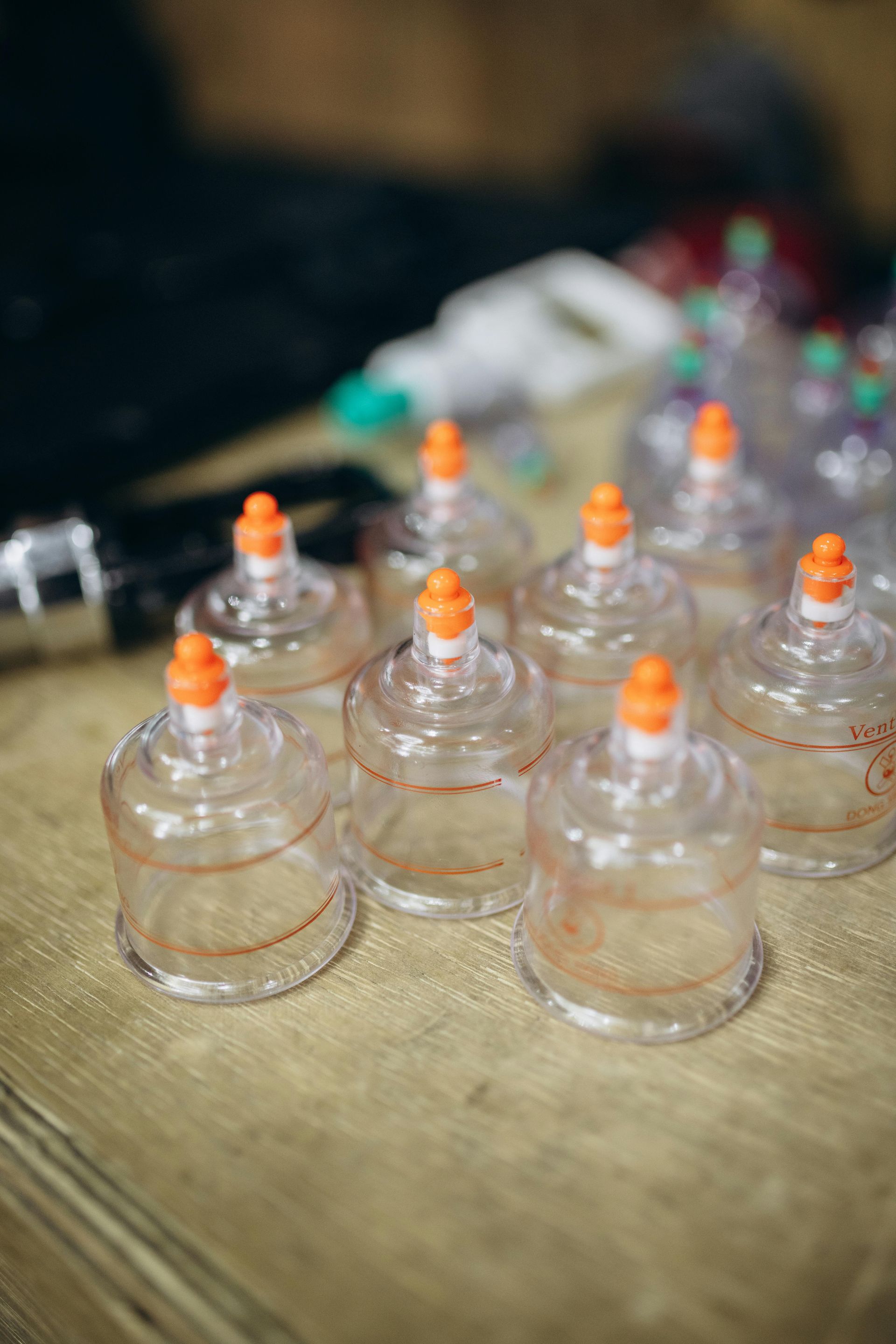 Clear cupping therapy cups with orange tops on a wooden surface.