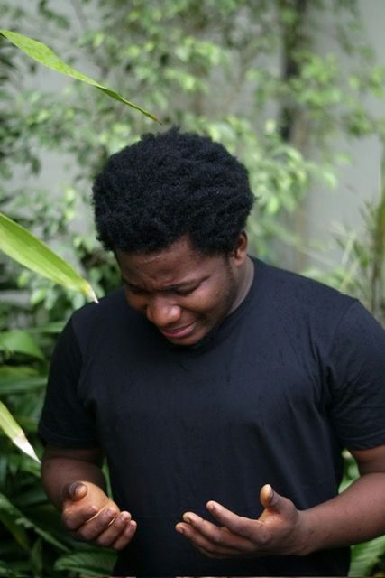 A man in a black shirt is standing in front of a tree