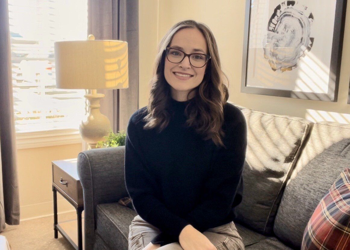 A woman wearing glasses is sitting on a couch in a living room.