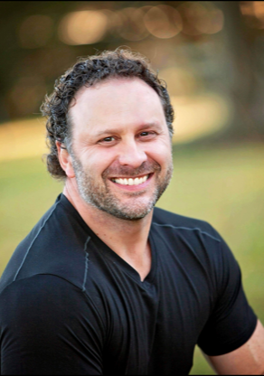 A man with a beard is smiling for the camera while wearing a black shirt.