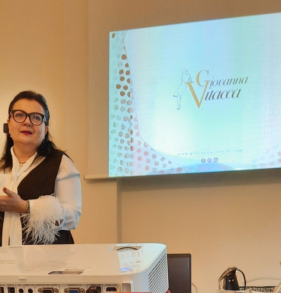 Una donna tiene una presentazione accanto a uno schermo con il nome