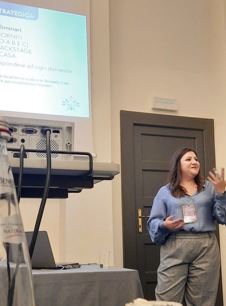 Donna che tiene una presentazione a una conferenza, indicando una diapositiva proiettata.