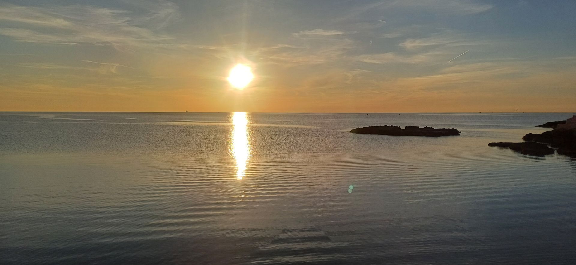 Tramonto su acque calme con il sole che si riflette sulla superficie.