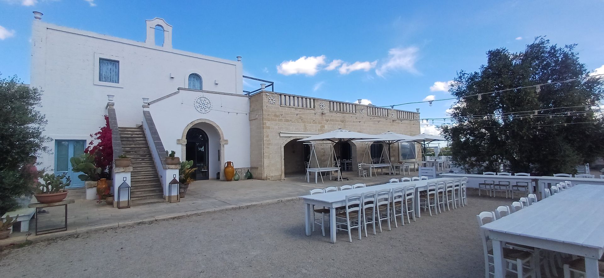 Edifici bianchi con archi e tavoli in un ambiente all'aperto sotto un cielo azzurro.