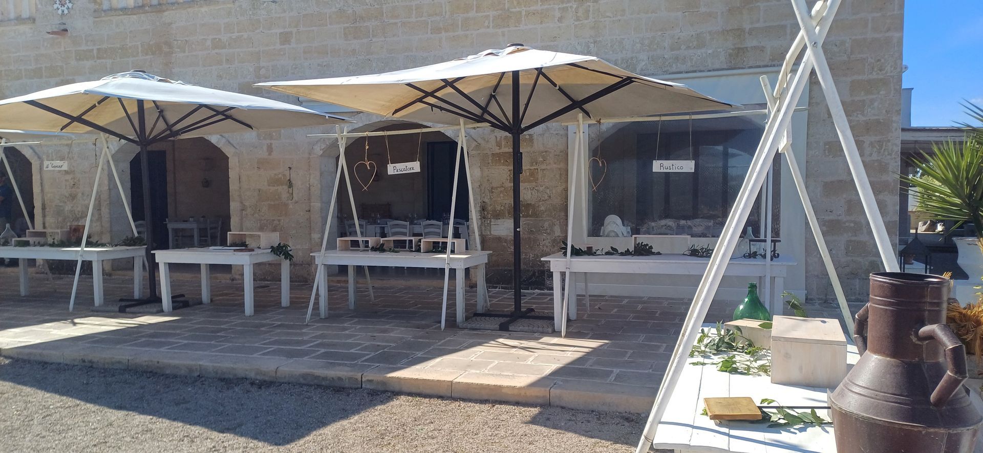 Tavoli all'aperto con ombrelloni di fronte a un edificio in pietra, esposizione di merci.