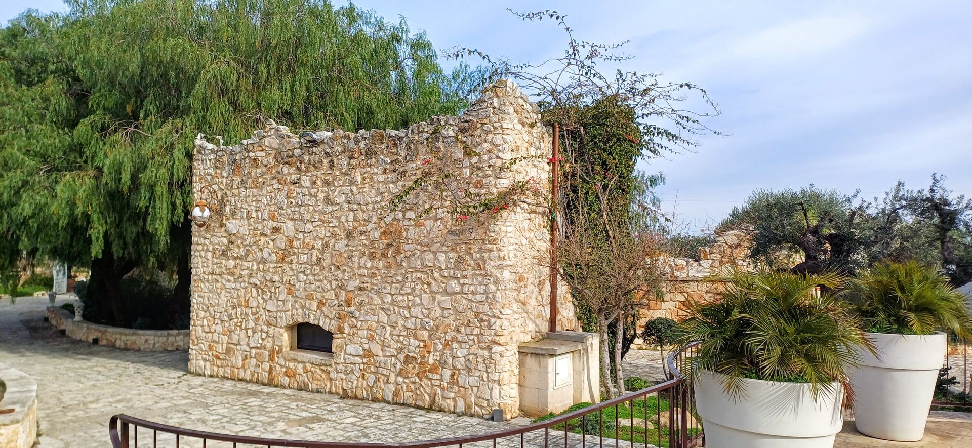 Edificio in pietra con un portale ad arco, circondato da fogliame e grandi fioriere bianche.