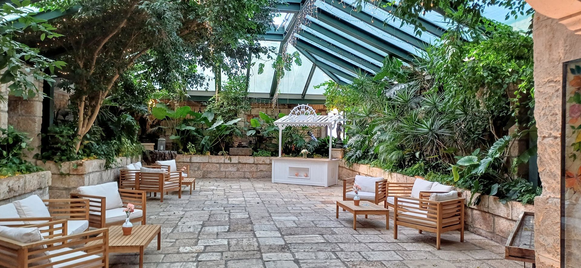 Un patio esterno lussureggiante e soleggiato, con mobili in legno e un gazebo bianco. Il verde circonda un vialetto in pietra.