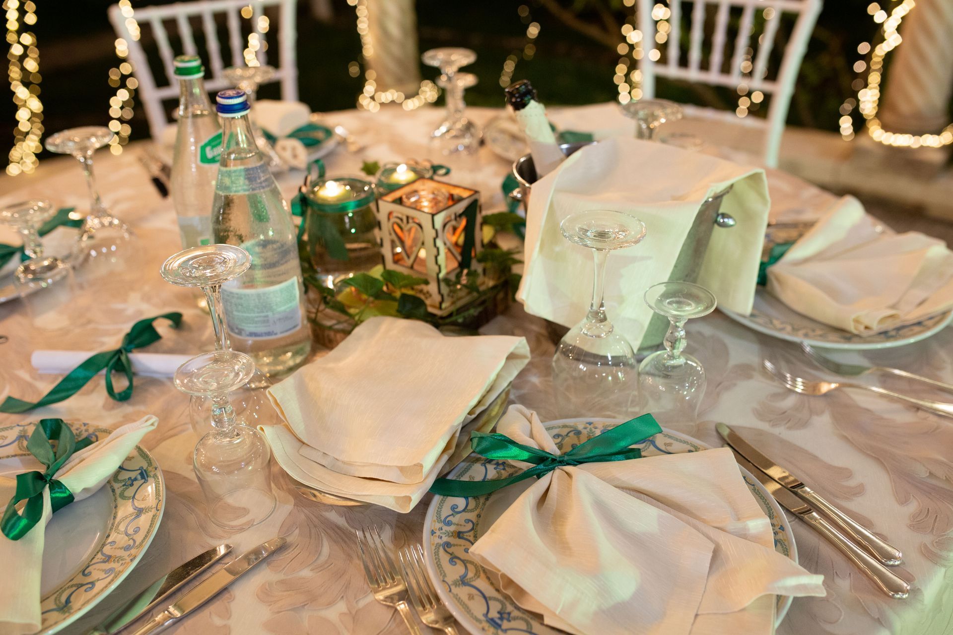 Elegante apparecchiatura con tovaglie bianche, dettagli verdi e candele per un evento speciale.