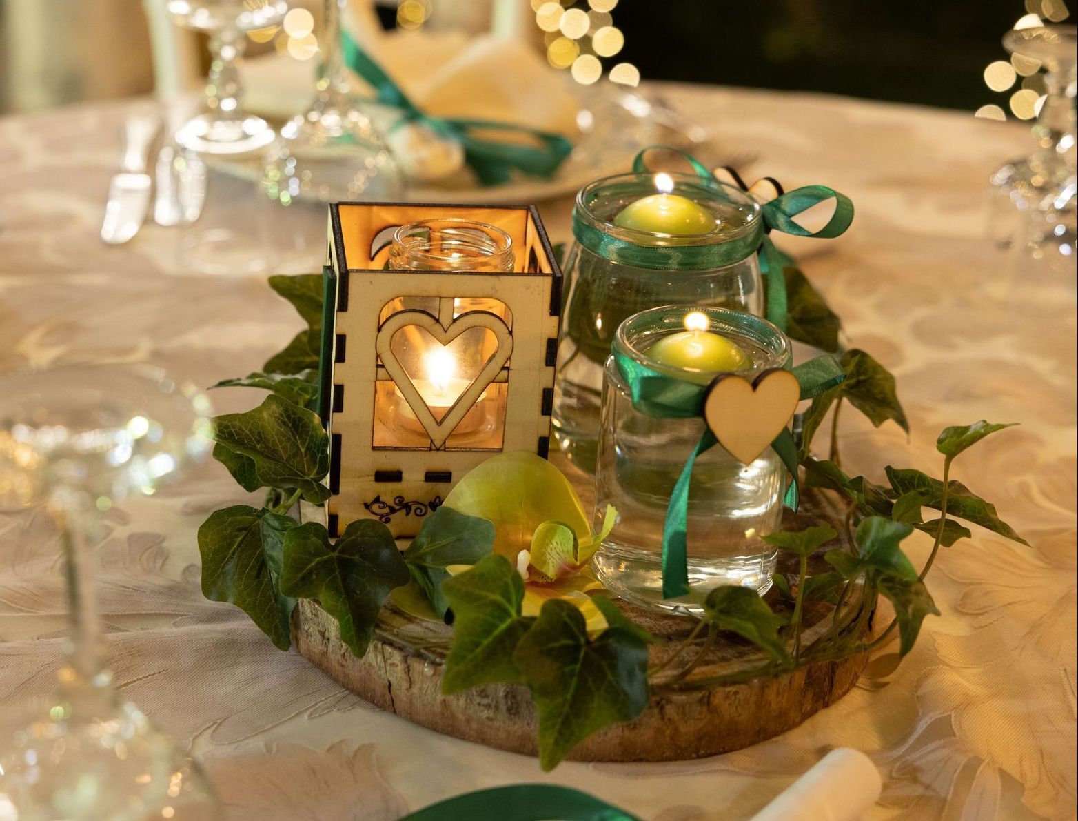 Centrotavola con candele, edera e dettagli in legno su un tavolo.