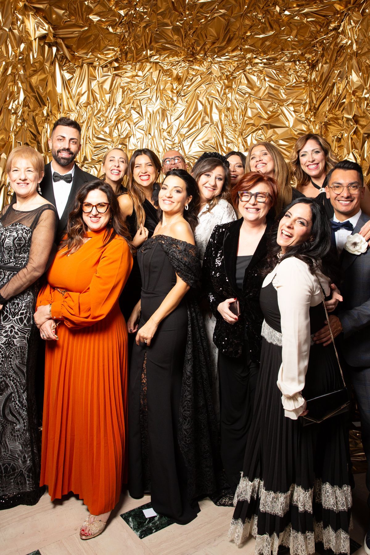 Un gruppo di persone in abiti formali posano sorridenti davanti a uno sfondo dorato.