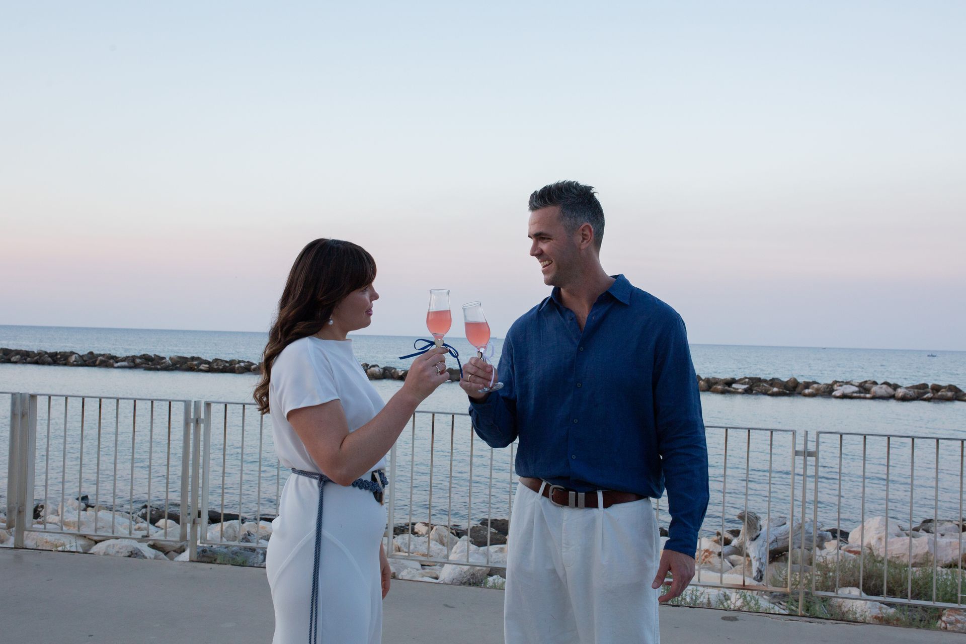 Coppia che brinda con drink rosa in riva all'oceano al tramonto.
