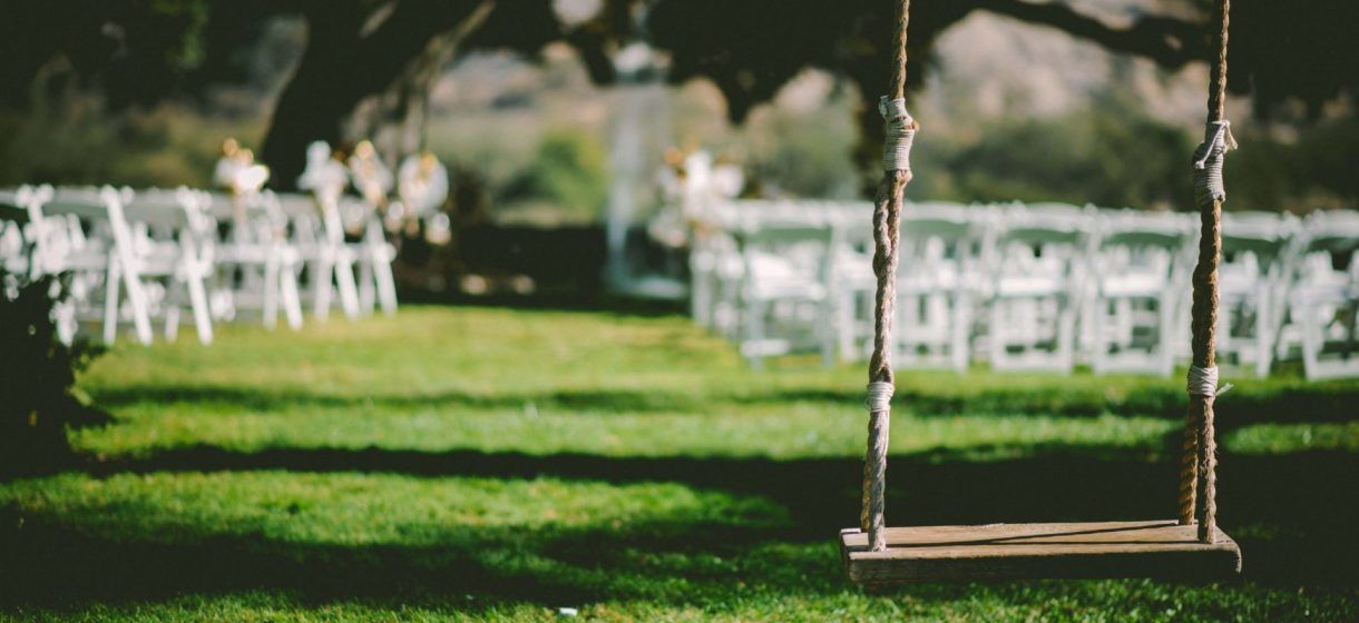 Altalena in legno sull'erba verde, file di sedie bianche che conducono a un altare, location per matrimoni all'aperto e soleggiata.