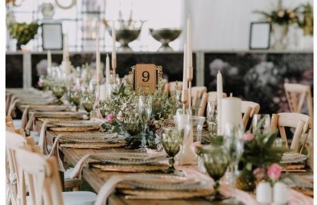 Lungo tavolo apparecchiato per un matrimonio, con centrotavola floreali, candele e calici verdi.