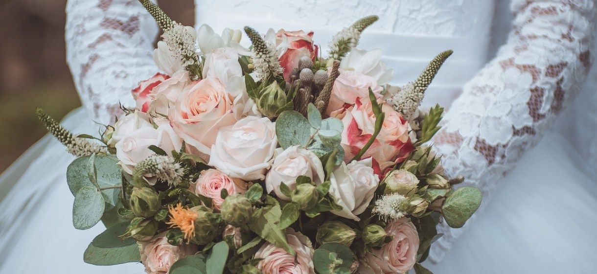 Una sposa con un abito di pizzo bianco che tiene in mano un colorato bouquet di rose e verde.