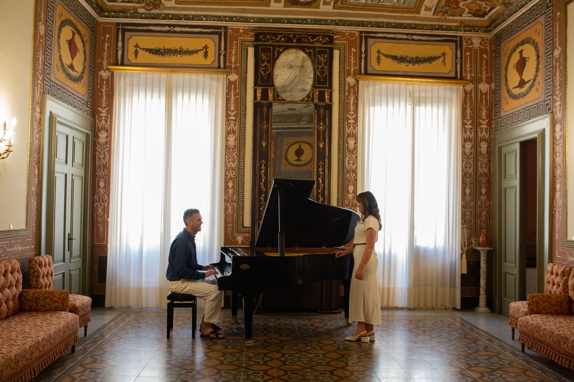 Coppia vicino a un pianoforte a coda in una stanza decorata con grandi finestre.