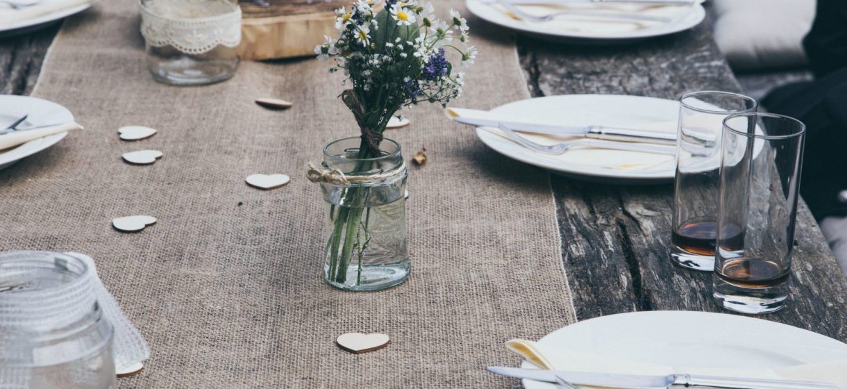 Apparecchiatura rustica da tavola con fiori in un piccolo barattolo, piatti bianchi e bicchieri.