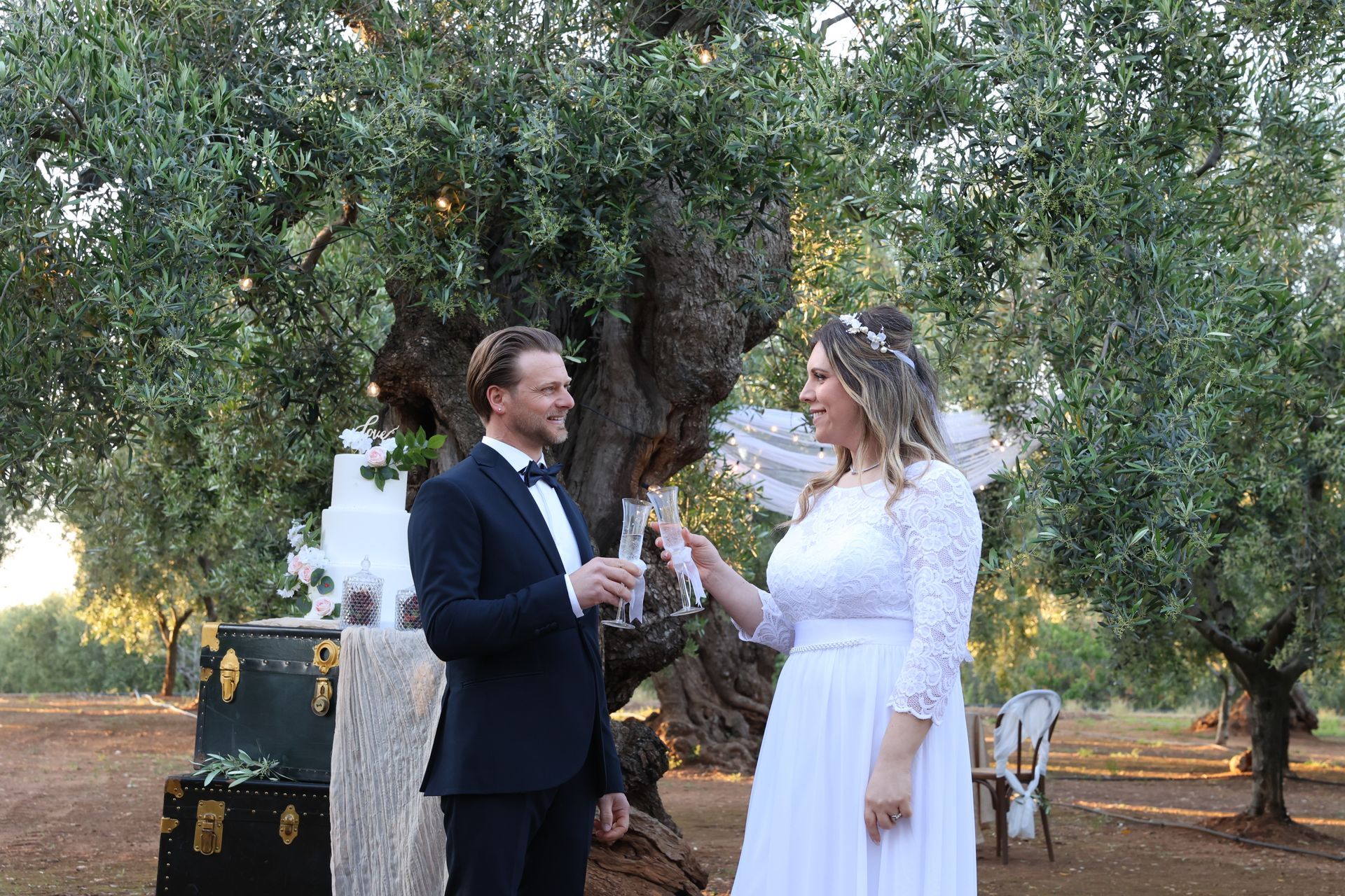 Coppia che brinda con champagne a un matrimonio all'aperto sotto un grande albero.