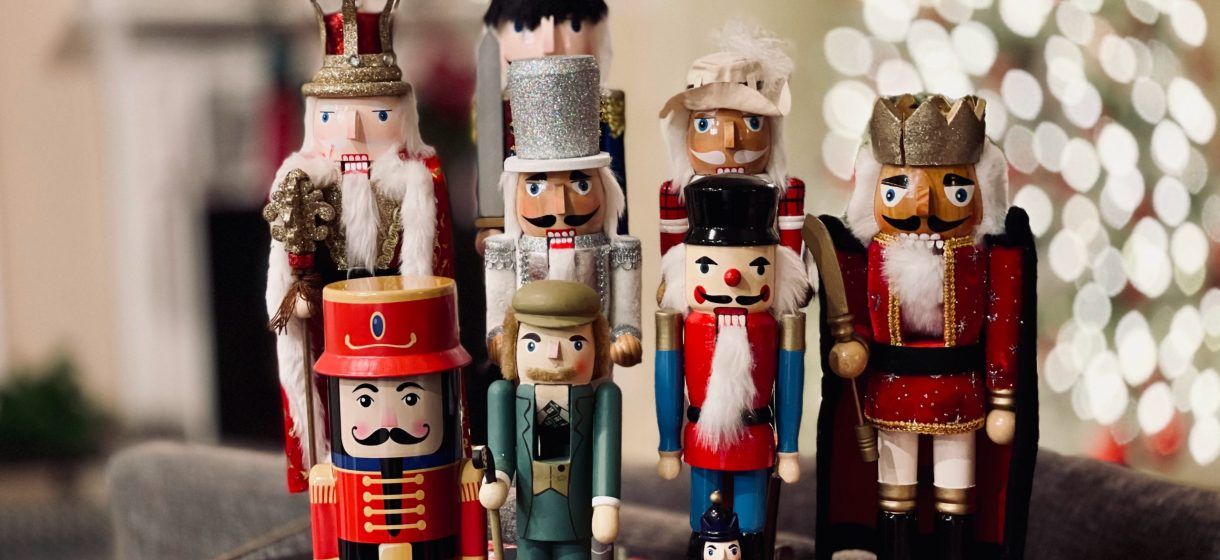 Collezione di schiaccianoci natalizi di varie dimensioni e con diverse decorazioni. Sullo sfondo, un albero di Natale sfocato.