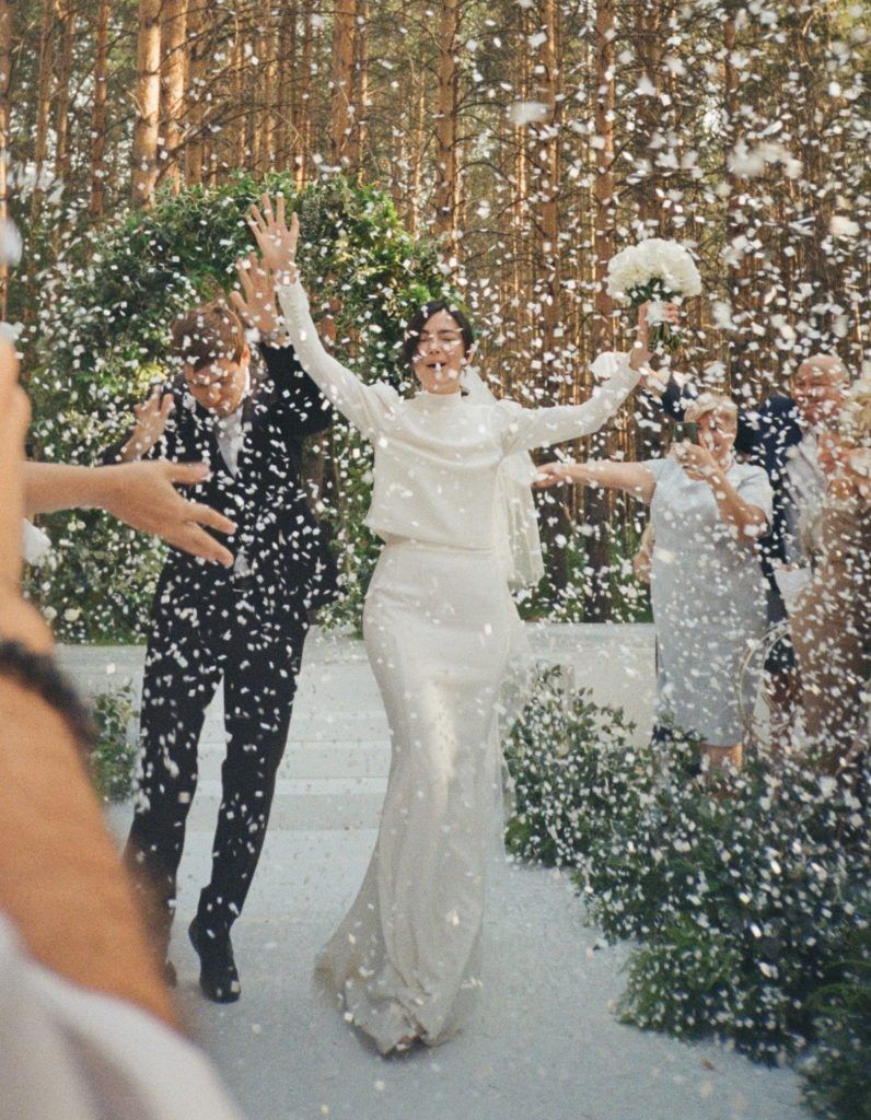 Gli sposi applaudivano mentre cadevano i coriandoli. La sposa indossava abito bianco e scialle. Lo sposo era in abito elegante. Scenario nella foresta.