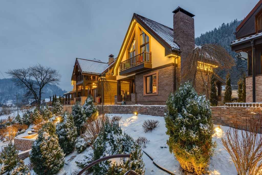 Case di lusso innevate con luci scintillanti in un ambiente invernale montuoso.
