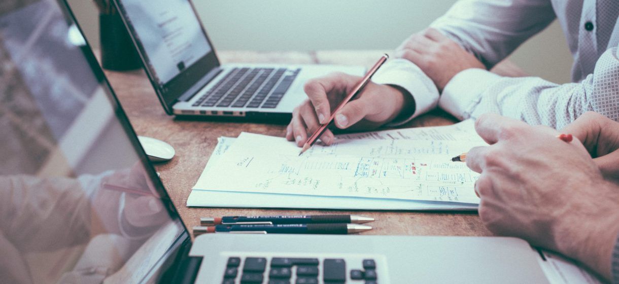 Due persone lavorano insieme a un documento con i loro computer portatili su una scrivania di legno.