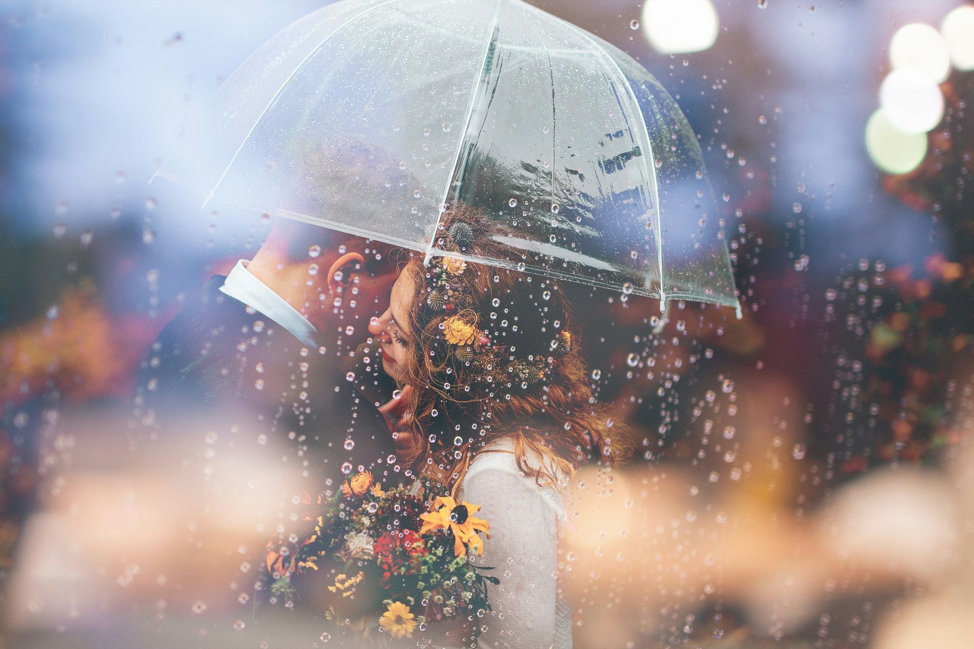 Coppia che si bacia sotto un ombrello trasparente sotto la pioggia, la sposa tiene in mano il bouquet.