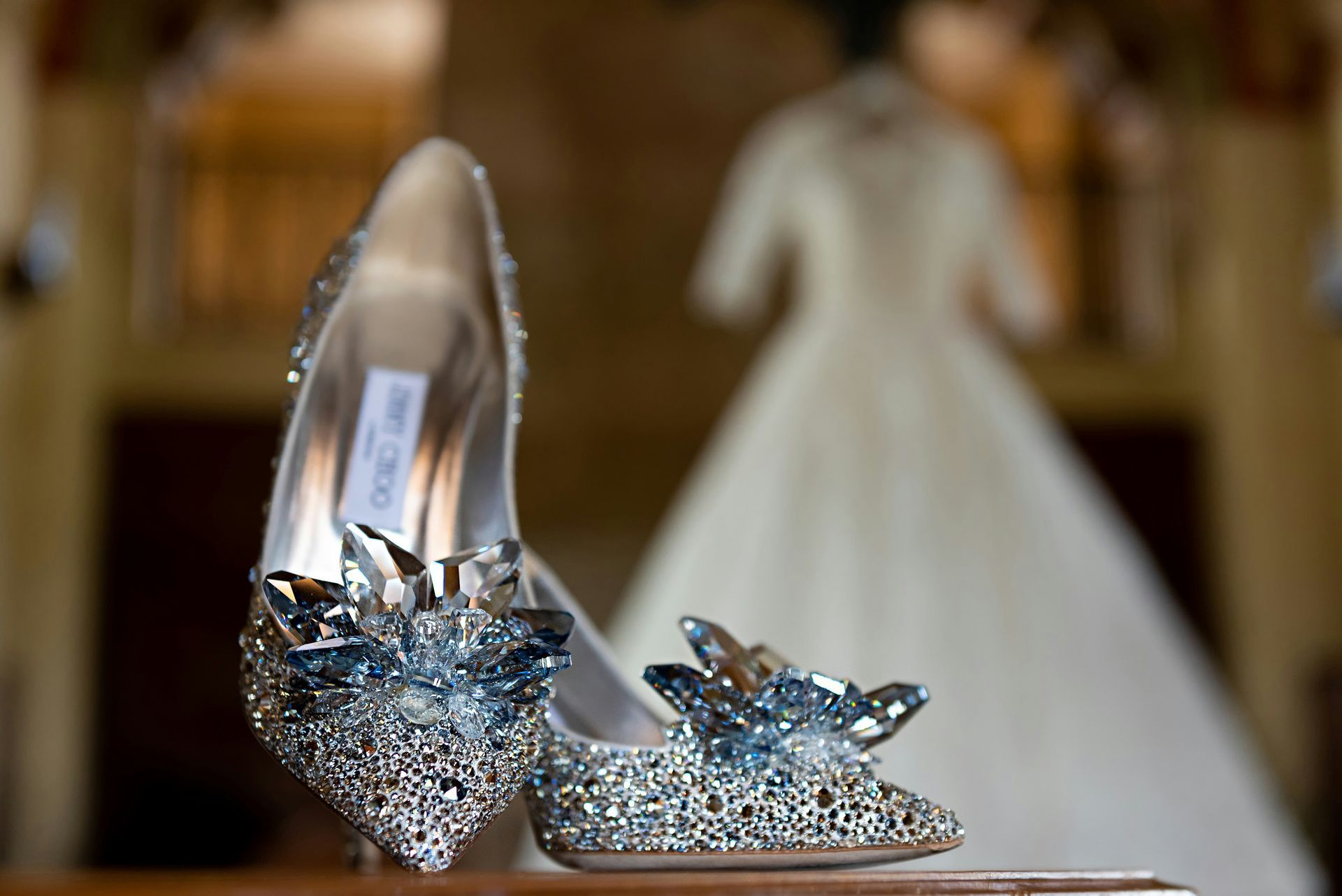 Scarpe da sposa color argento scintillante con dettagli in cristallo blu, abito sfocato sullo sfondo.