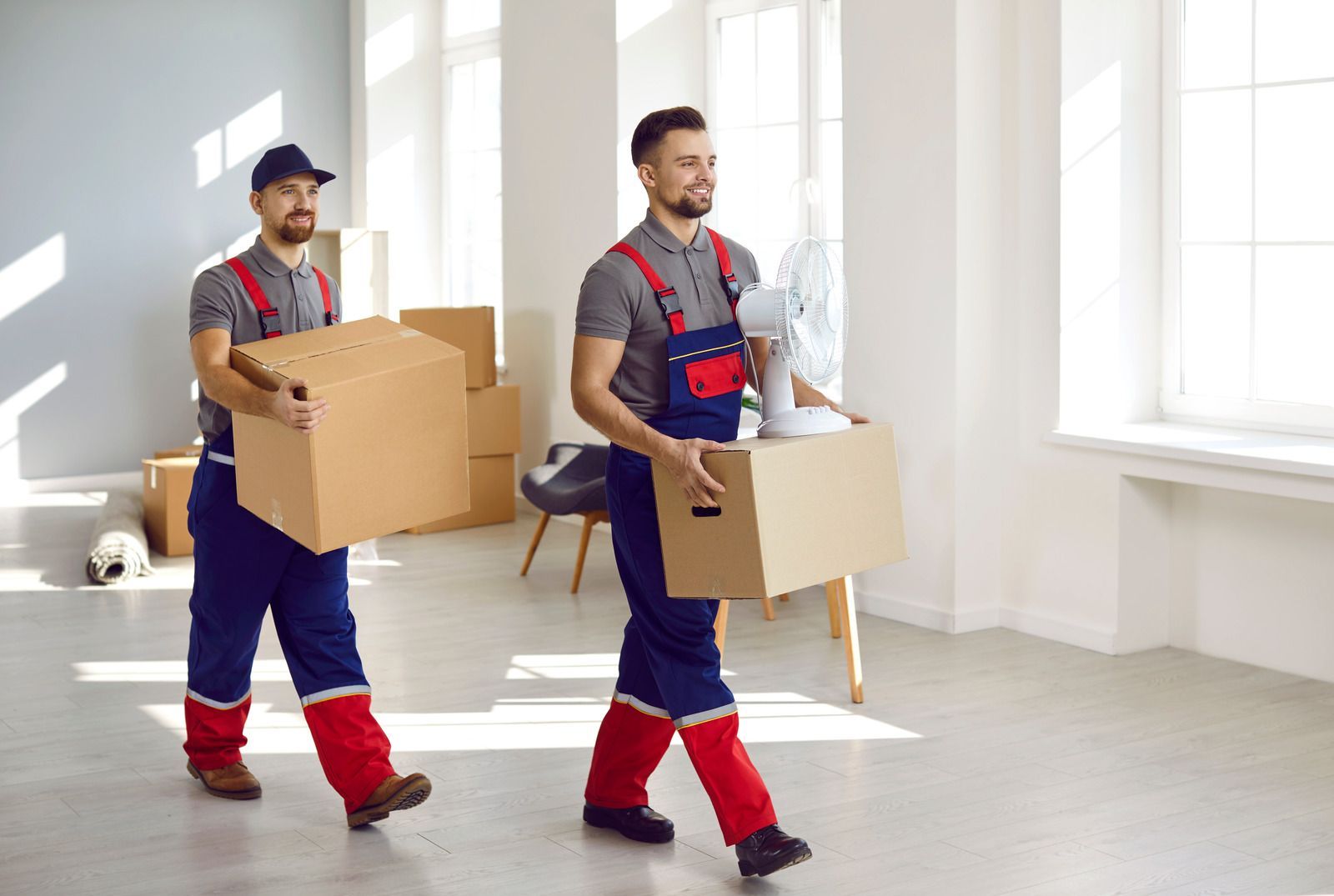 Two men are carrying boxes in an empty room.