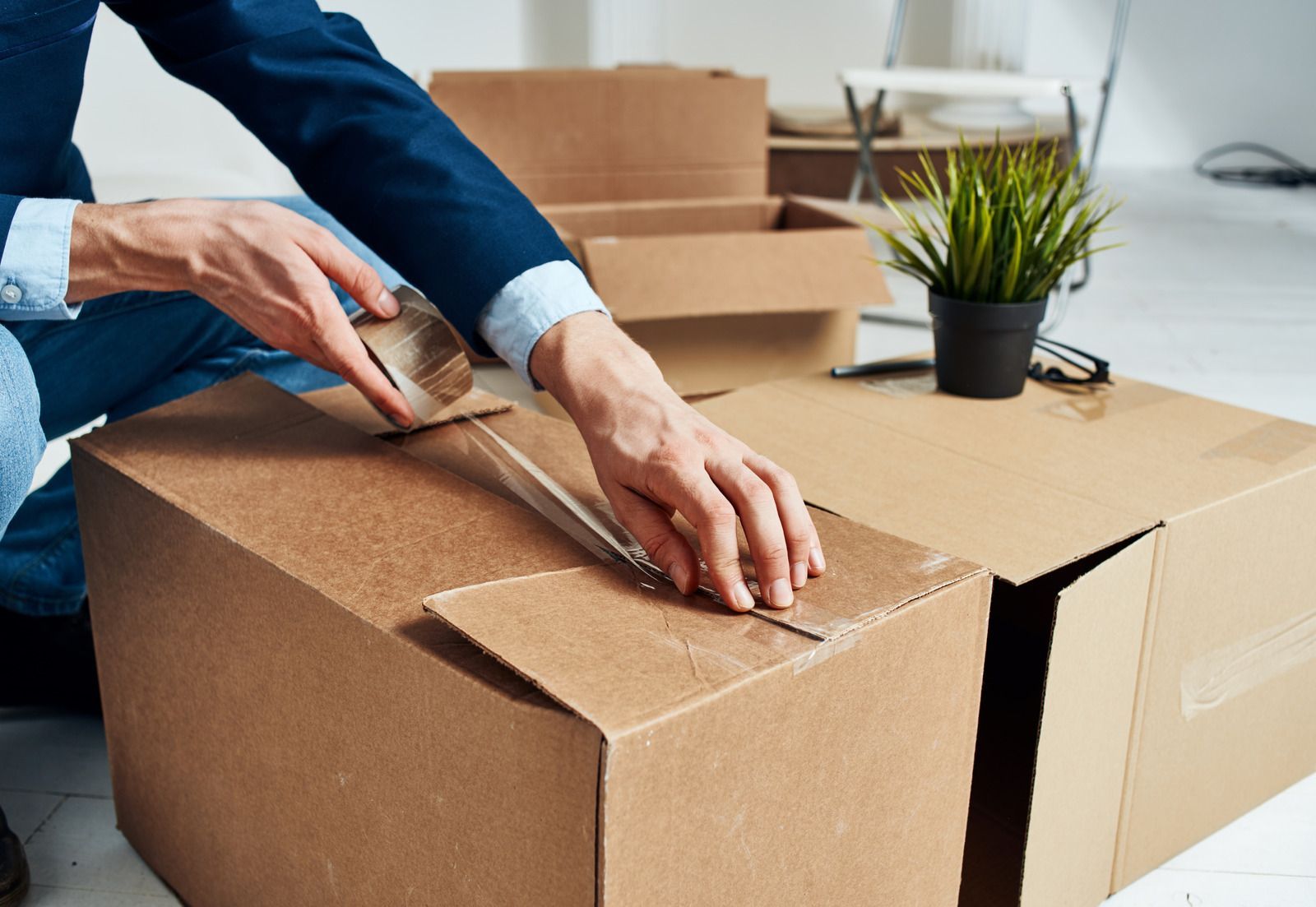 A man is sitting on the floor wrapping a cardboard box with tape.