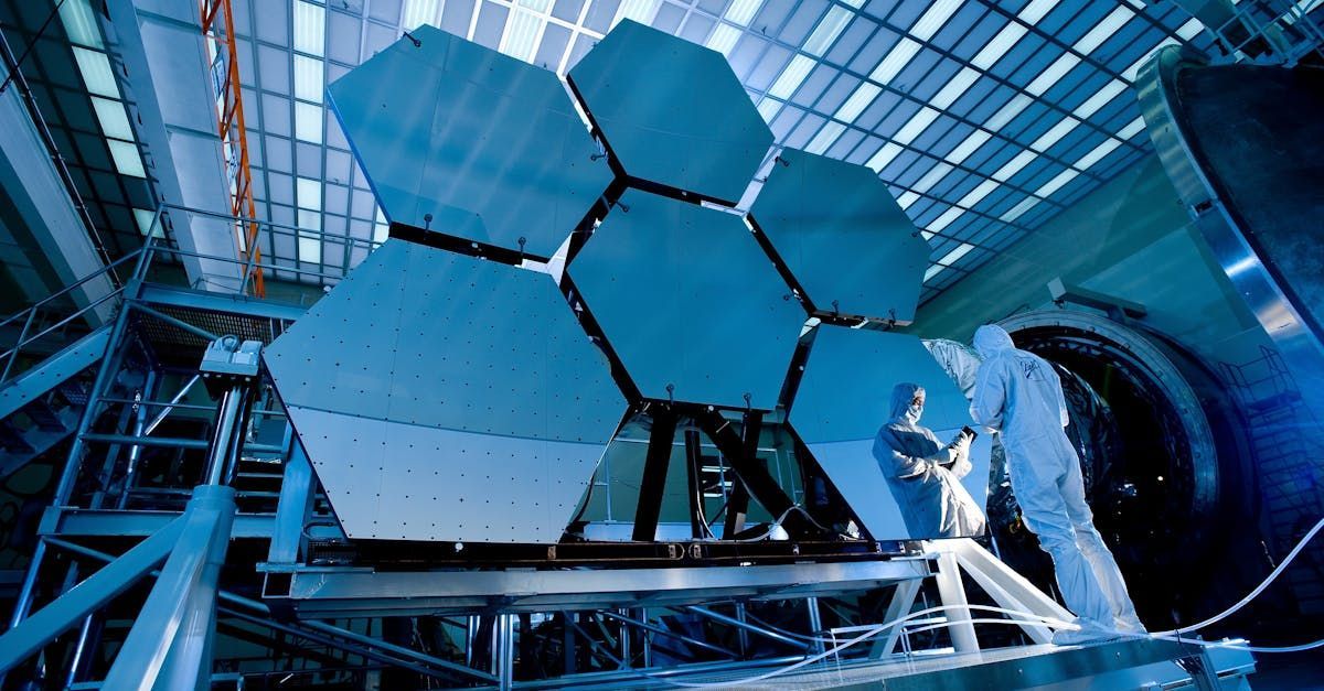 A man in a white suit is standing in front of a large hexagon shaped object.