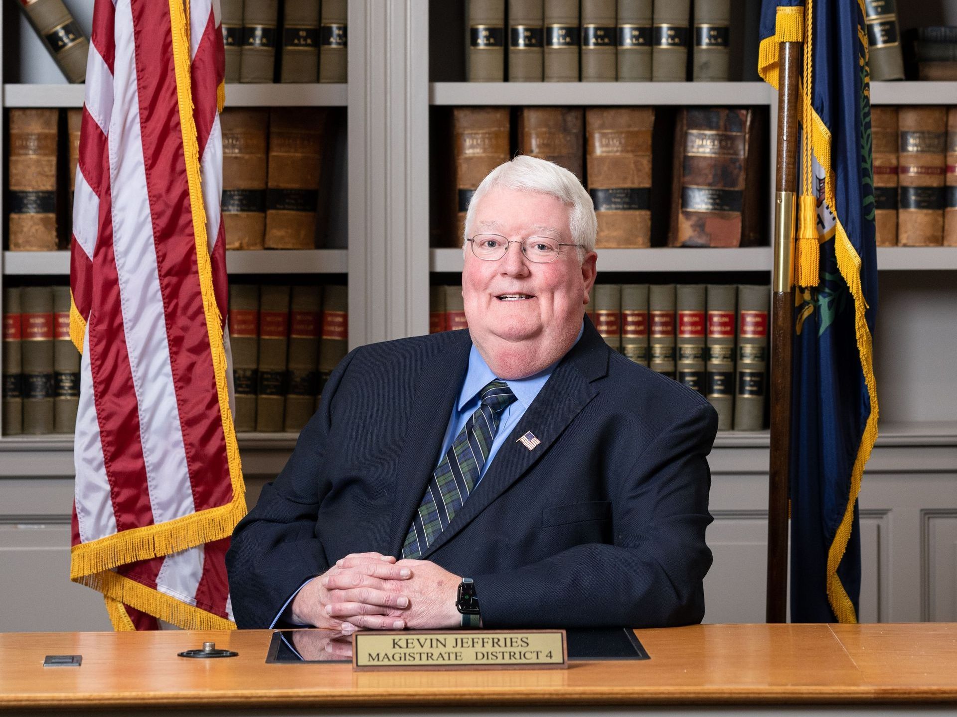 A man in a suit and tie is sitting at a desk in front of an american flag.