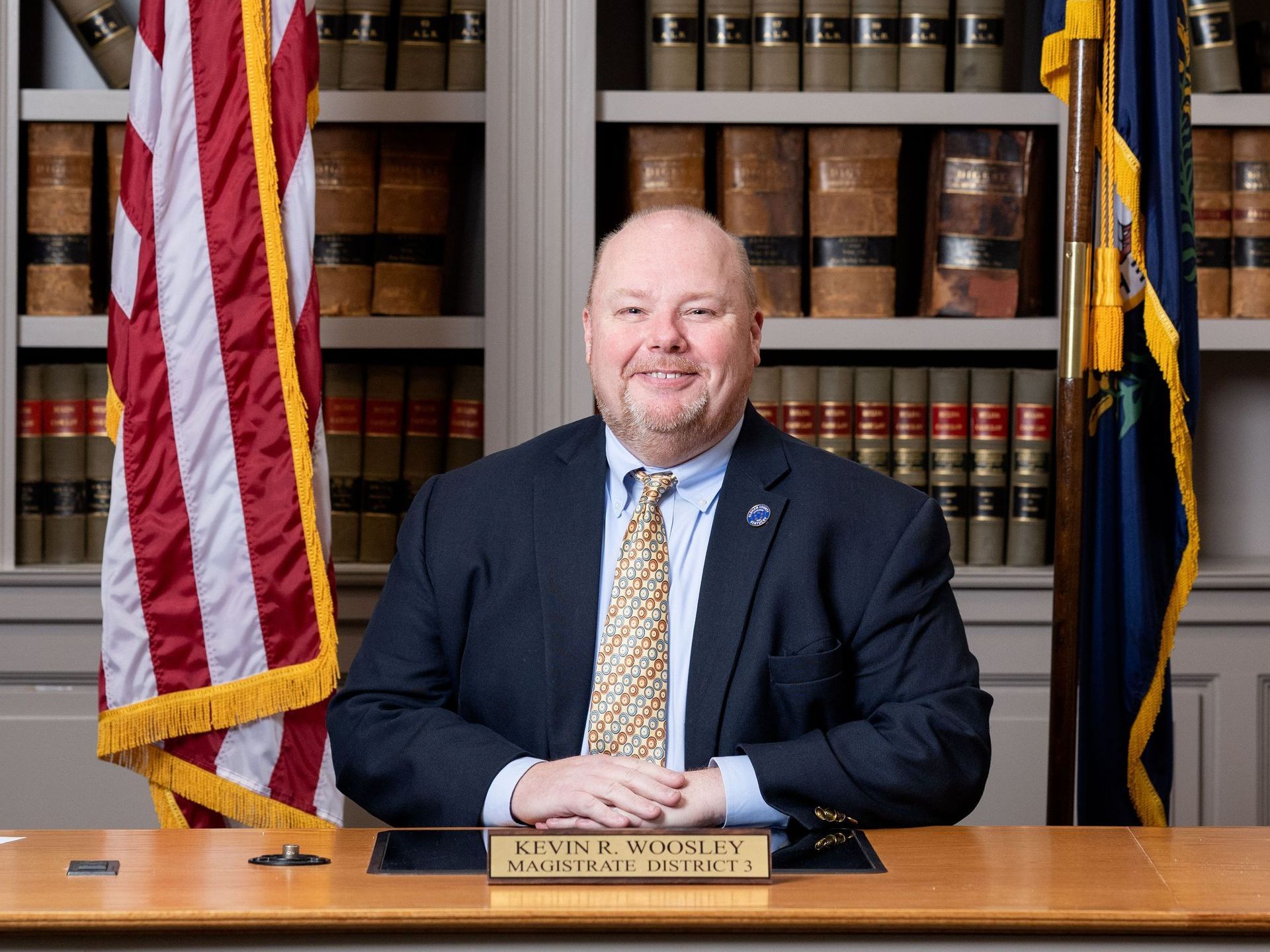 A man in a suit and tie is sitting at a desk in front of an american flag.