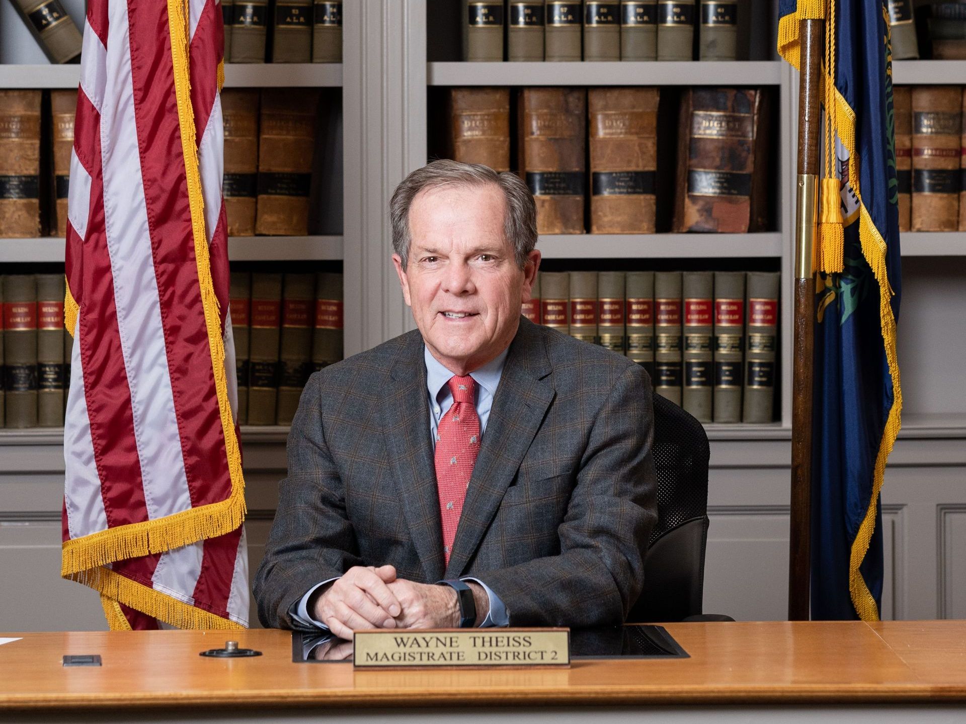 A man in a suit and tie is sitting at a desk with a name plate that says wayne tells