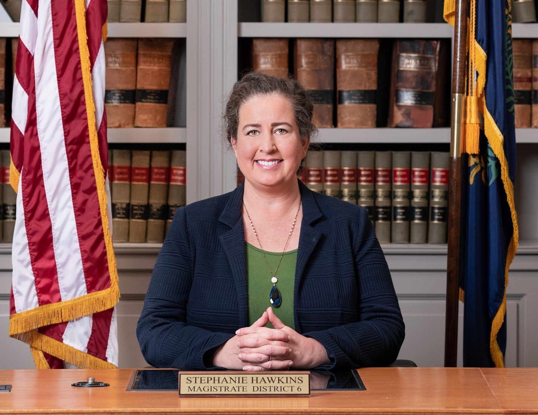 A woman is sitting at a desk in front of an american flag.