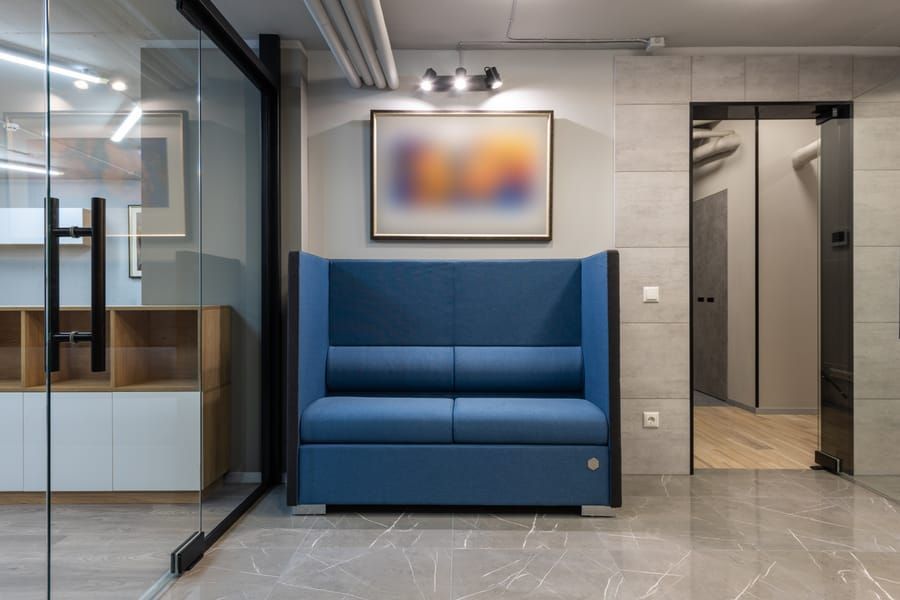 Blue two-seat bench in a modern office lounge beside glass walls and an elevator