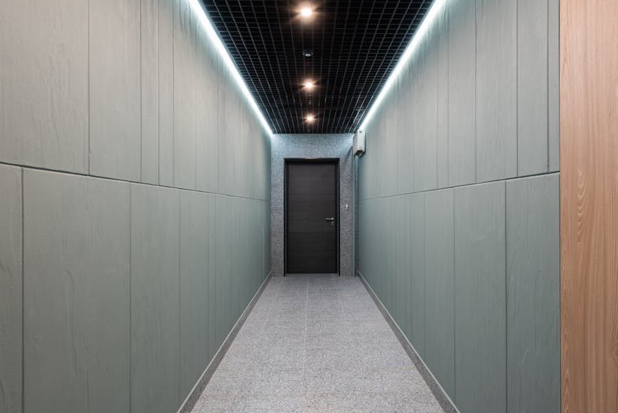 Modern hallway with gray walls, black ceiling lights, and a closed door at the end