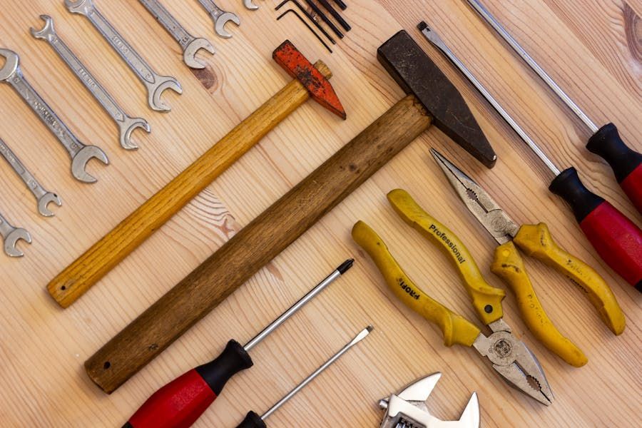 Assorted hand tools on a wooden surface, including hammers, wrenches, screwdrivers, and pliers.