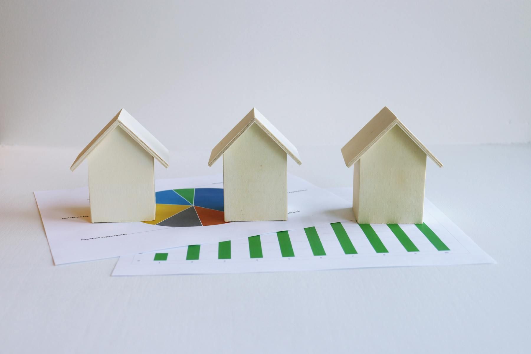 Three small white paper houses on a white surface, with a green-striped road in front.