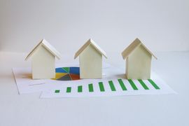 Three small white paper houses on a white surface, with a green-striped road in front.