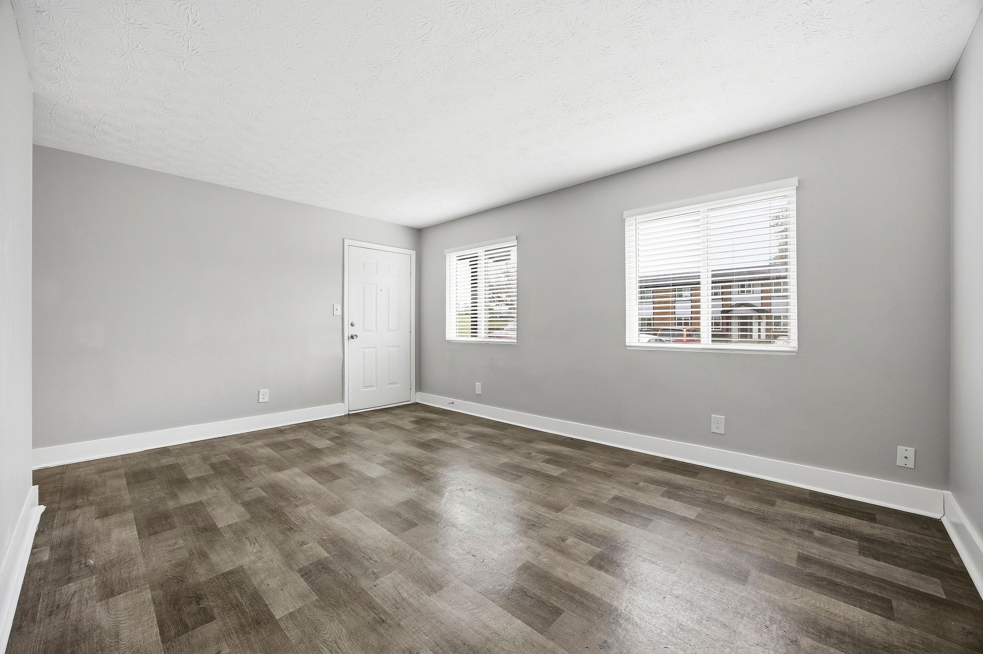 Empty gray living room with wood-look floor and two windows letting in daylight