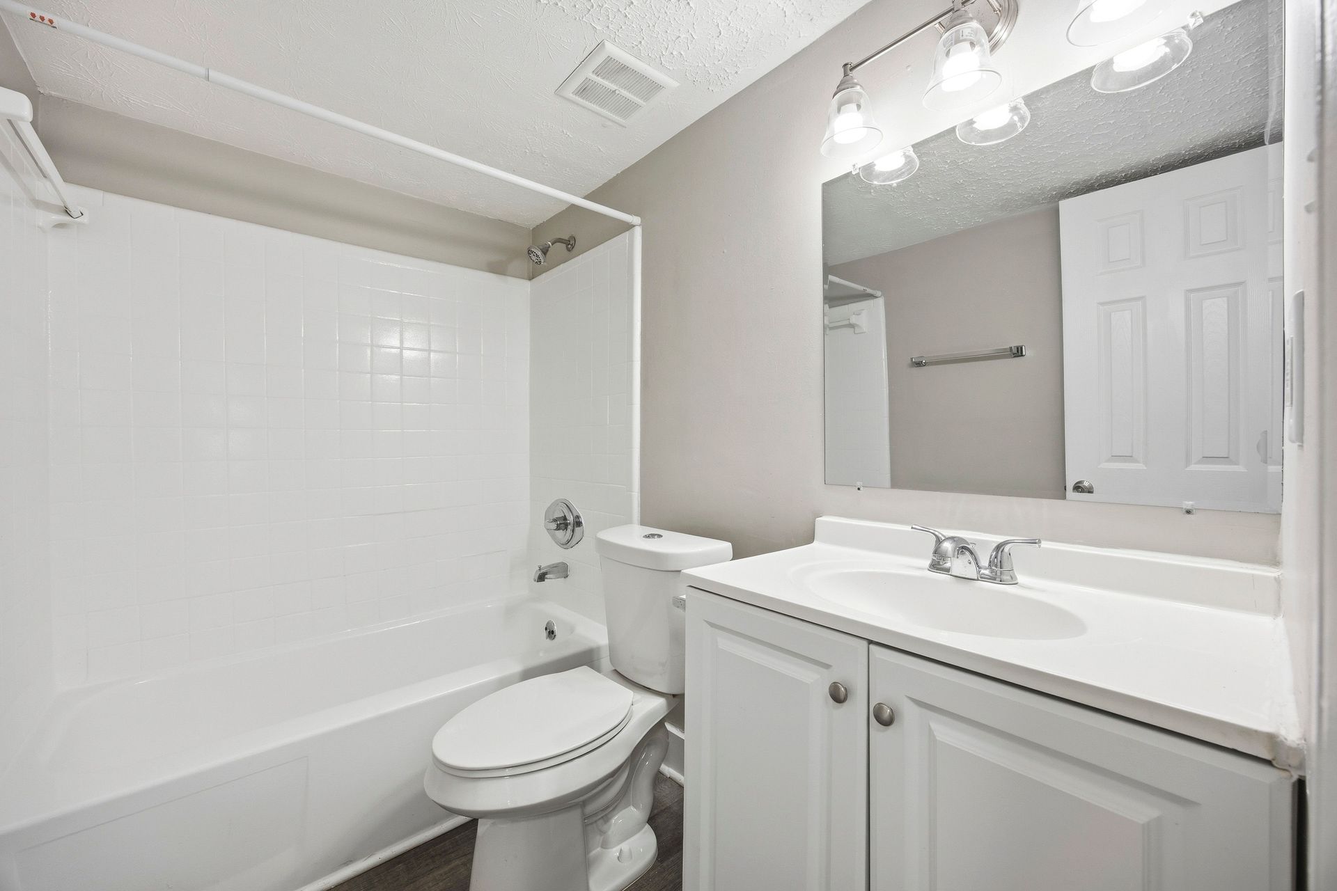 Bright white bathroom with tub, toilet, and vanity mirror.