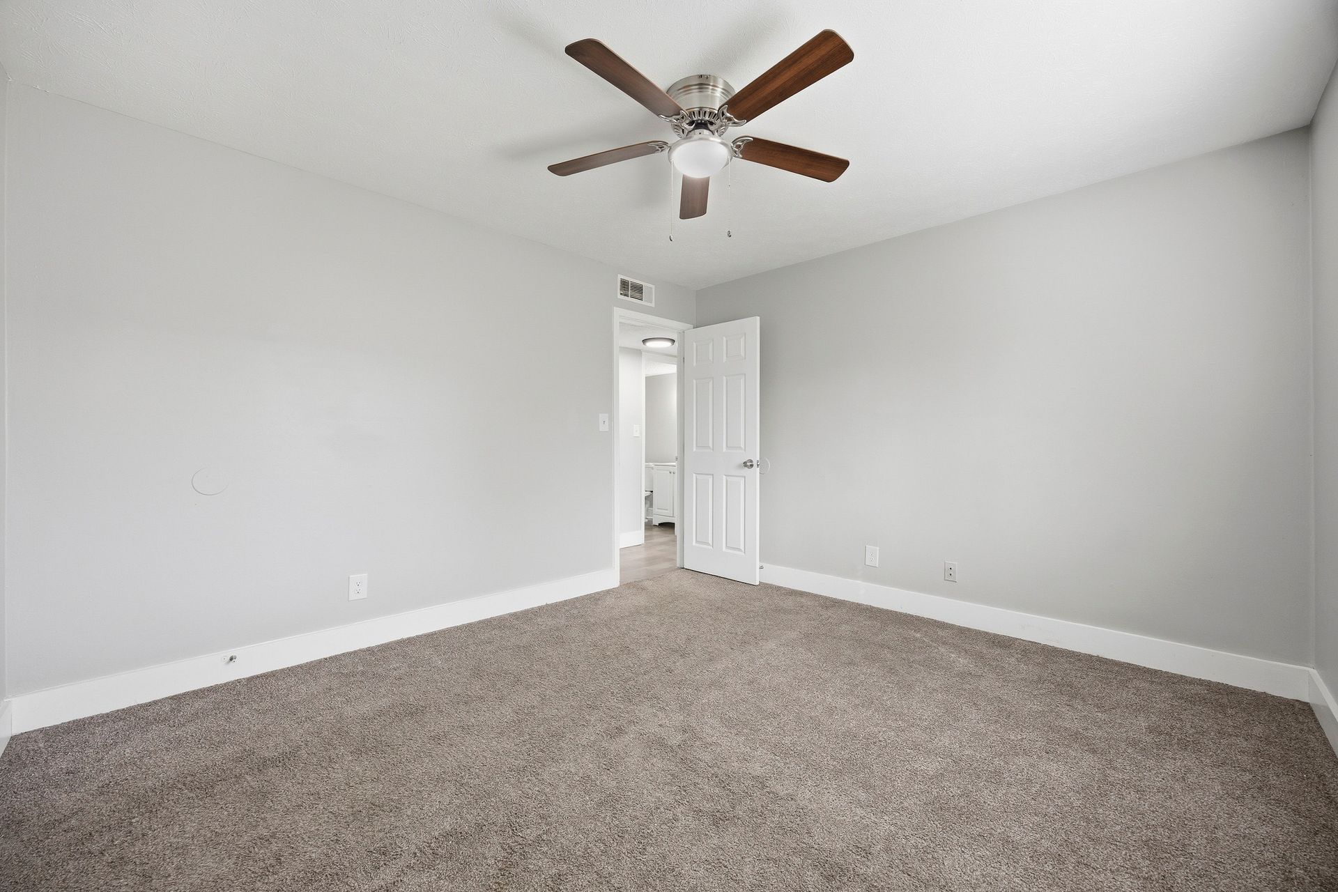 Empty bedroom with gray carpet, white walls, and a ceiling fan with wood blades