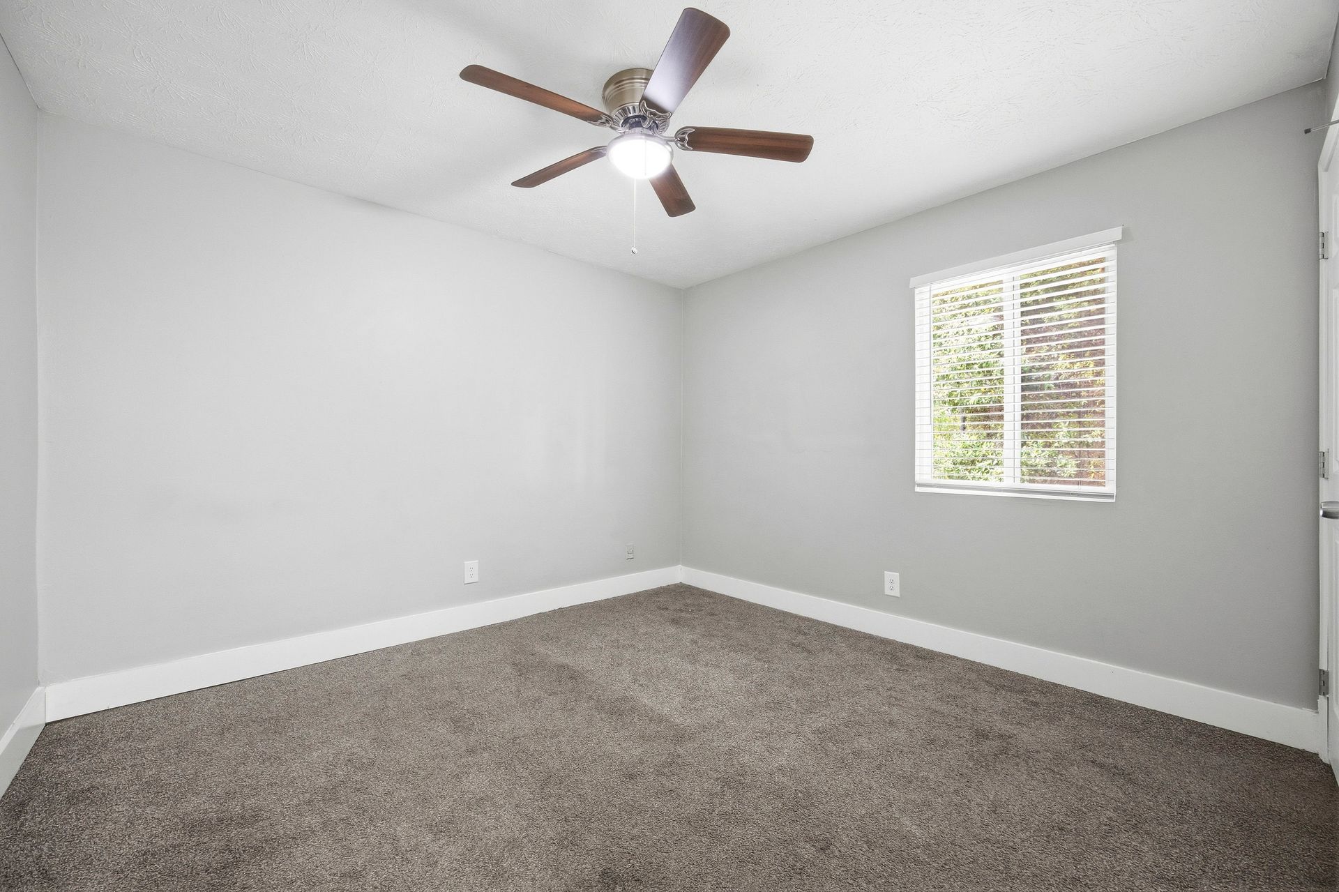 Empty gray bedroom with carpet, ceiling fan, and a small window with blinds