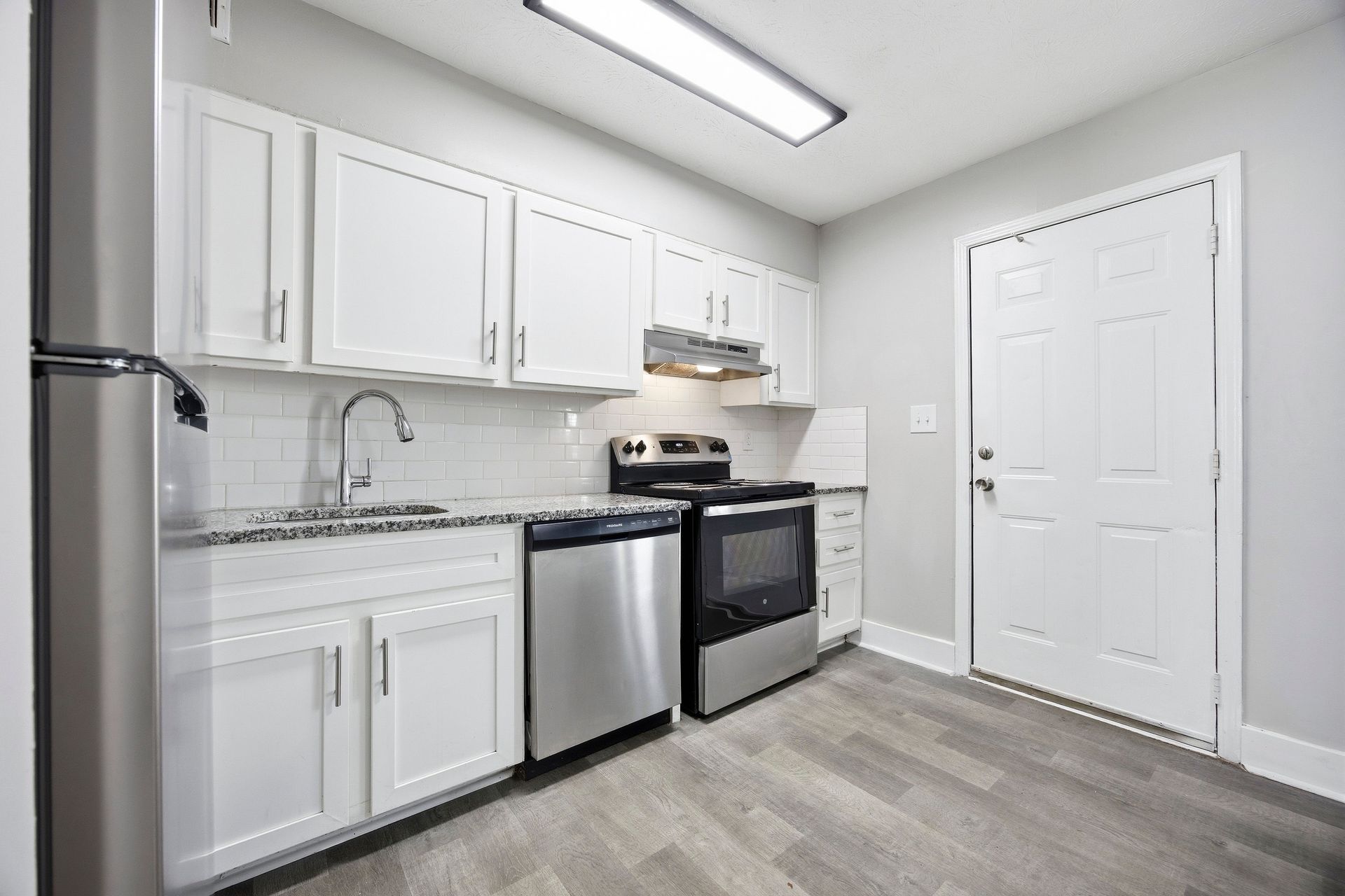 Bright white kitchen with stainless steel appliances, gray flooring, and white cabinets.