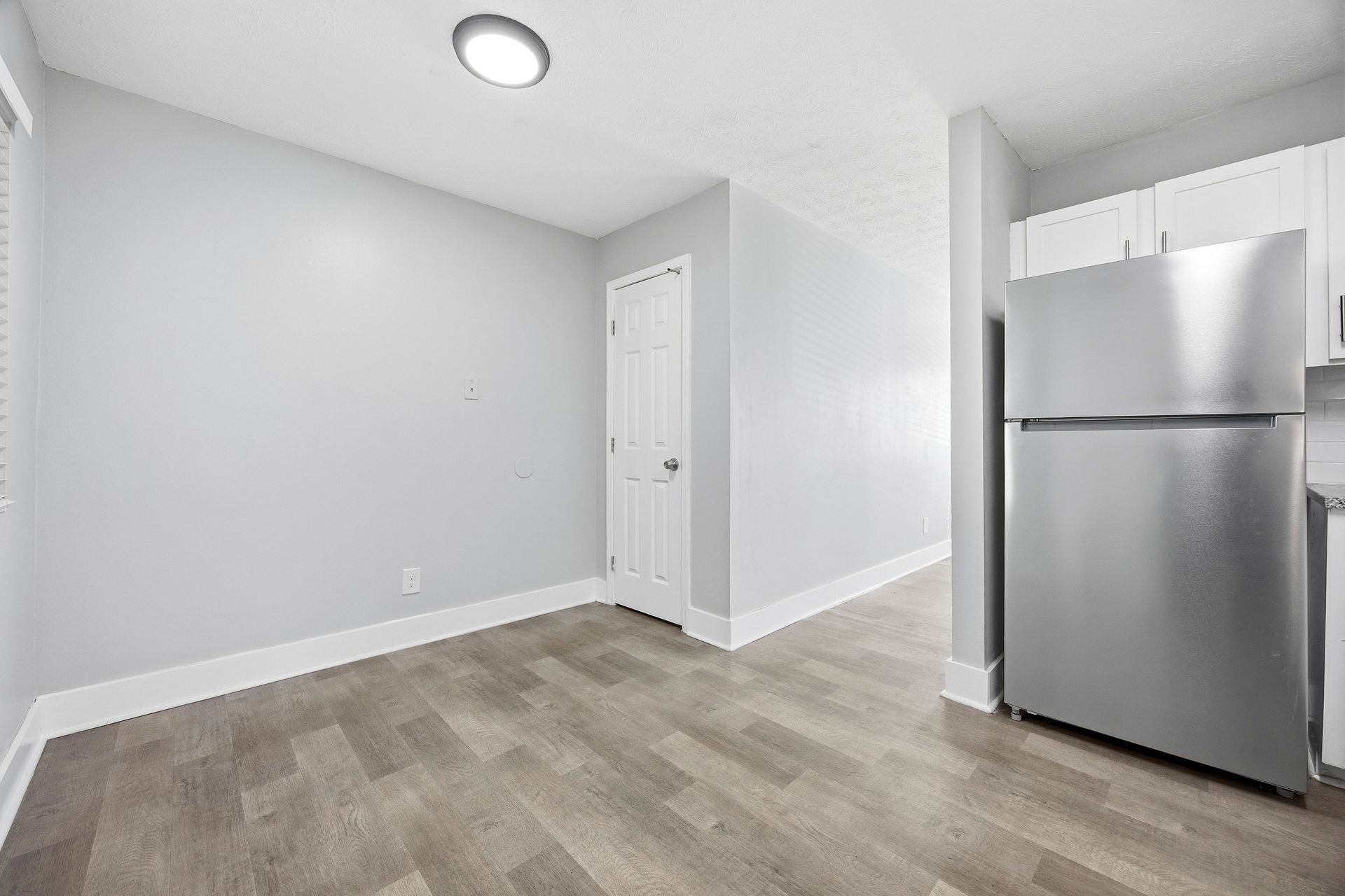 Empty gray room with wood-look floor, white door, and stainless steel refrigerator in the corner