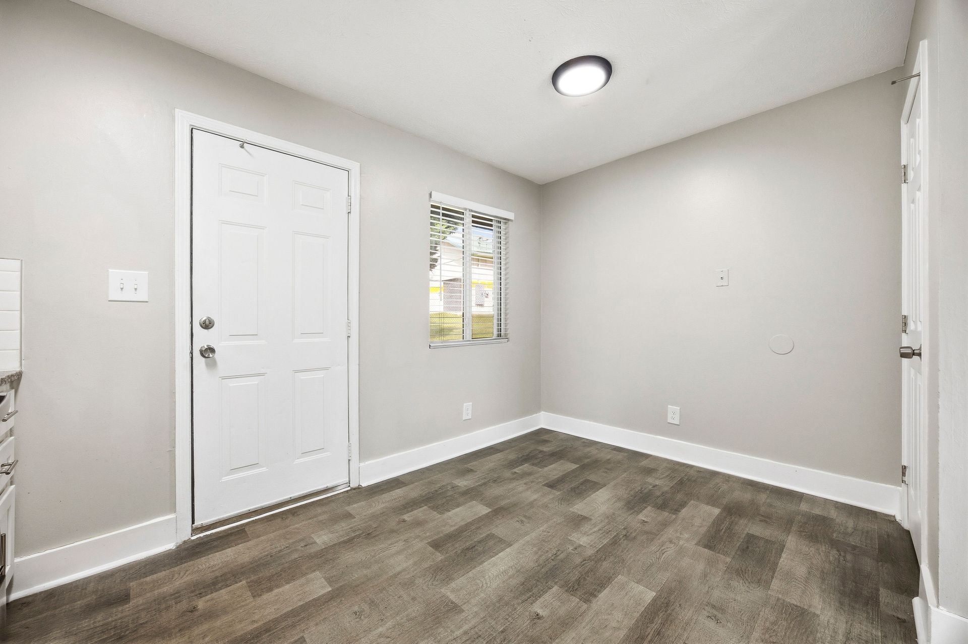 Empty light gray bedroom with carpet, white closet door, window, and ceiling light