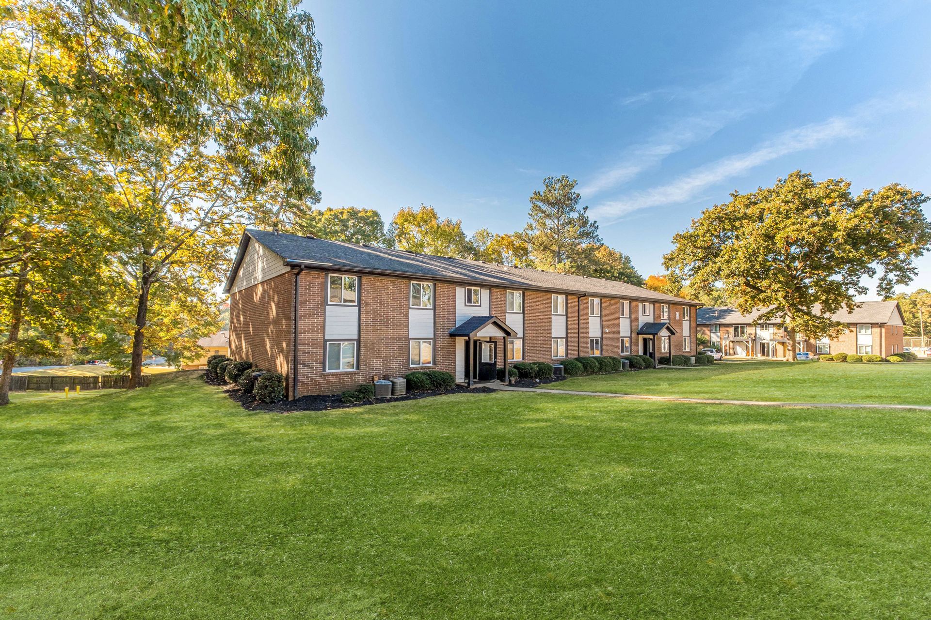 Brick apartment building with a large green lawn and trees under a blue sky