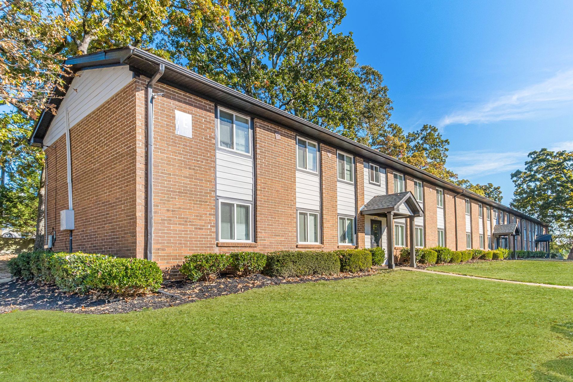 Brick apartment building with white-trimmed windows and a green lawn under a blue sky