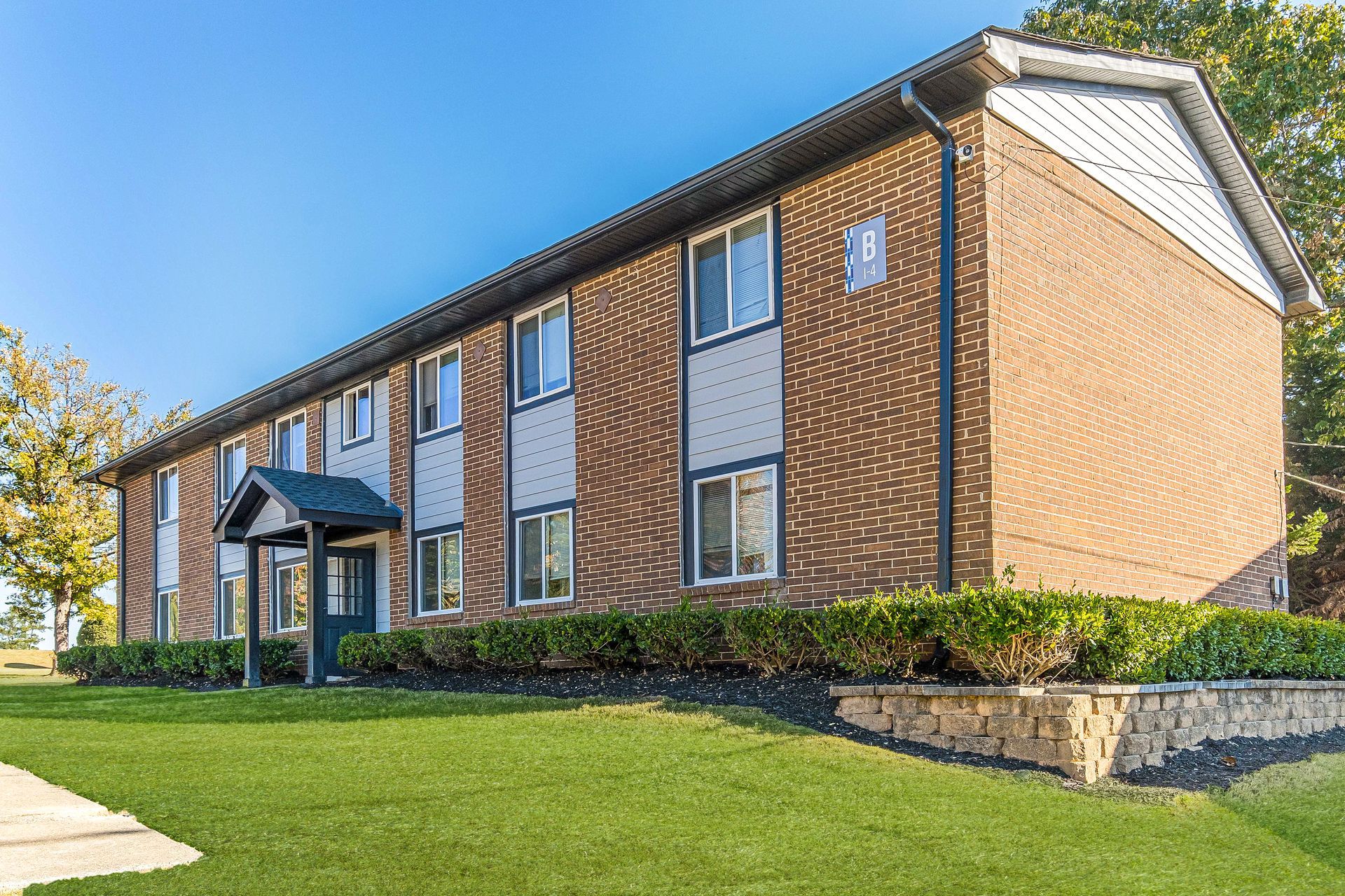 Brick apartment building with white trim and manicured lawn under a clear blue sky