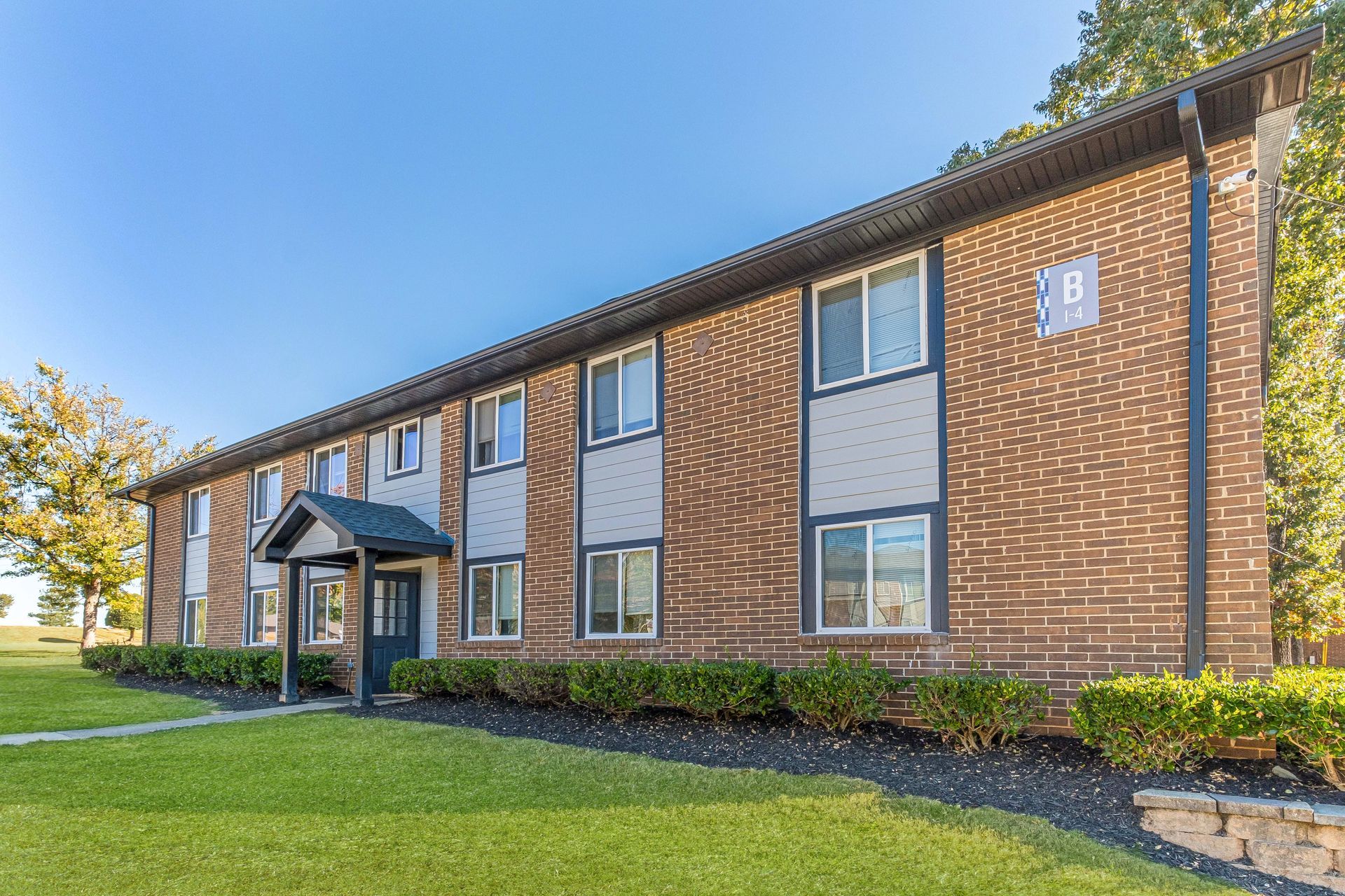 Two-story brick apartment building with a grassy lawn and blue sky